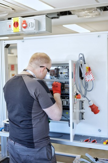 A man in a black shirt with red gloves working in a control panel.
