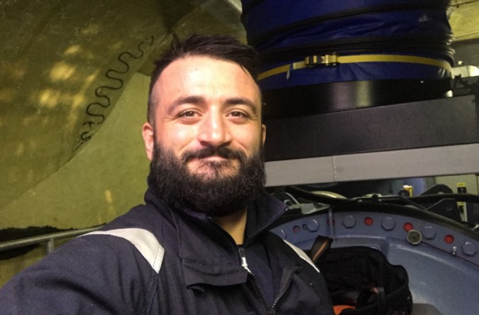A bearded man stands by a blue machine inside a wind turbine nacelle, reflecting on his journey as WTS founder Dominic Connolly.