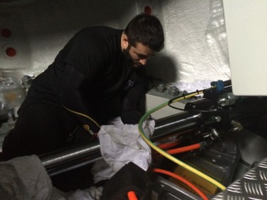 A man in a black shirt works intently on machinery with colorful cables in a dimly lit space, conveying focus and technical expertise.