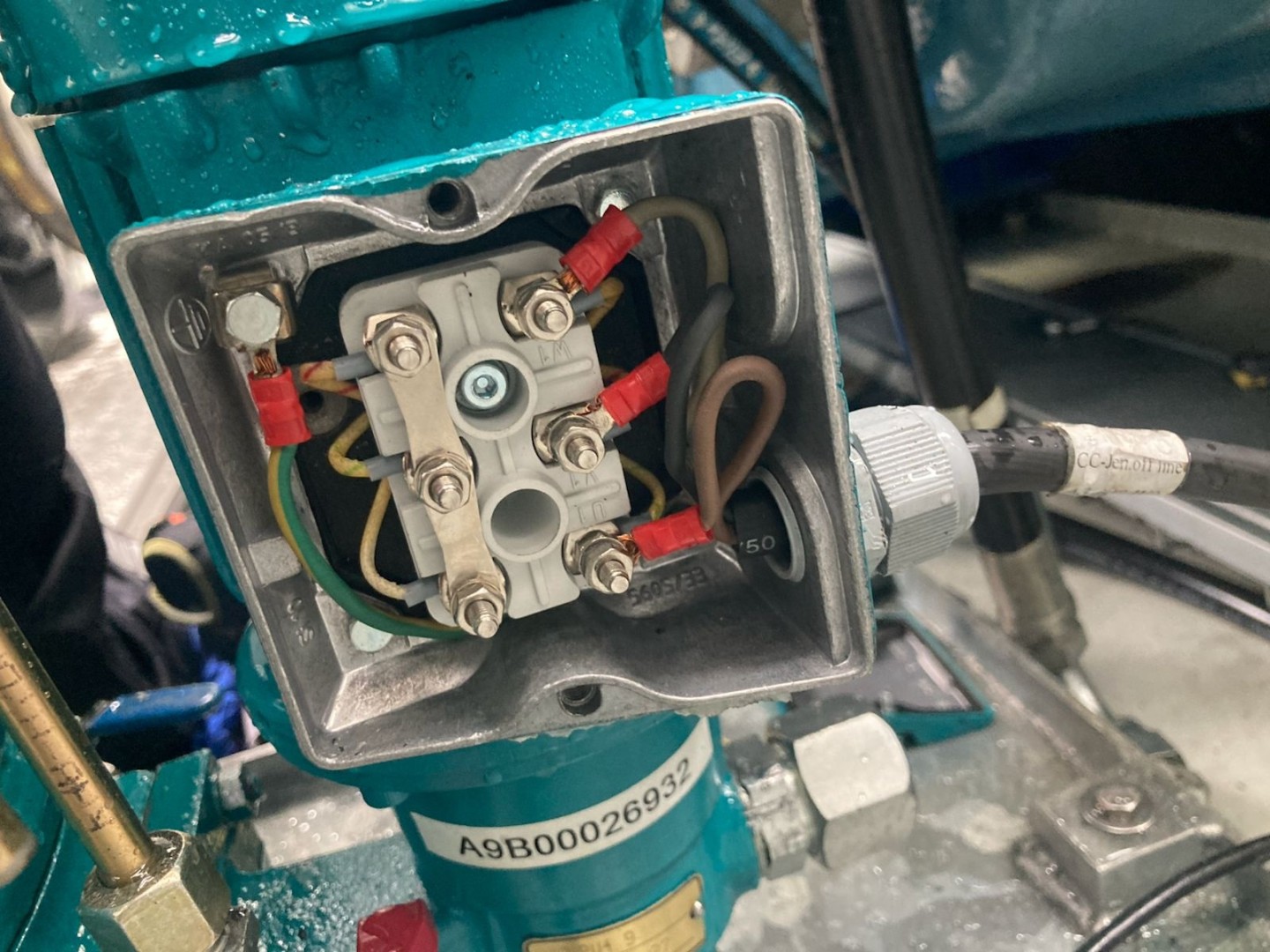 Open electrical junction box with visible wires, connectors, and screws. The blue background and industrial setting suggest machinery maintenance.