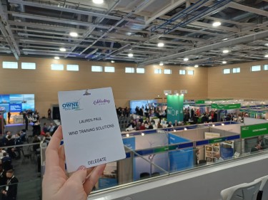 A delegate badge in front of the conference hall for OWNE 2025.