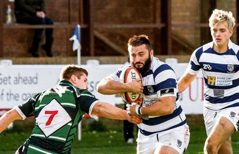 Dom playing rugby holding the ball, with a team mate behind and the opposing player attacking.